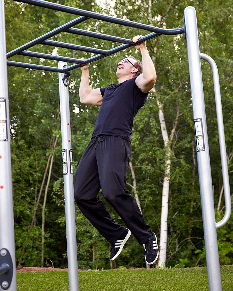 Ein Mann macht Klimmzüge an den Stangen eines Fitnessstudios im Freien.